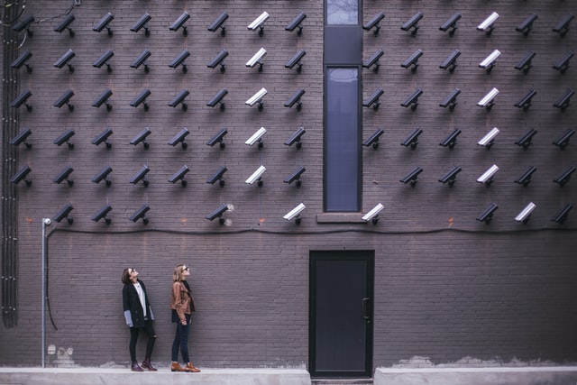 Picture of people looking at dozens of security cameras mounted on a wall